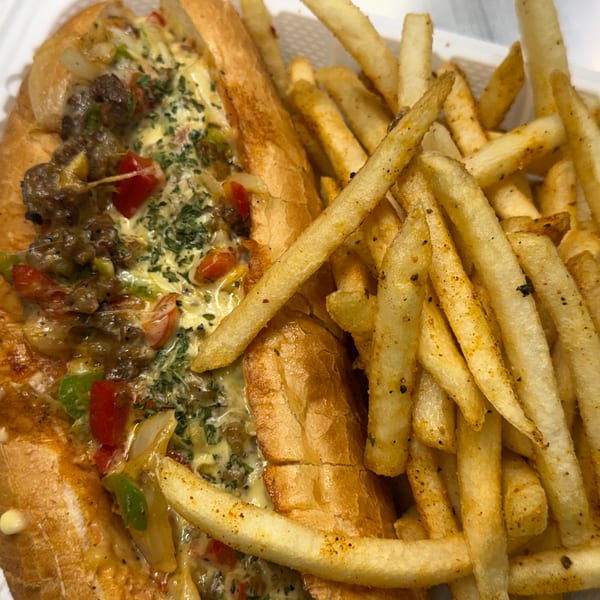 Loaded cheesesteak sandwich with melted cheese and vegetables, served with seasoned french fries.