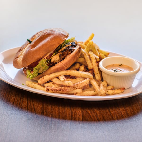 A juicy burger with lettuce, tomato, seasoned fries, and a side of creamy sauce on a white plate.
