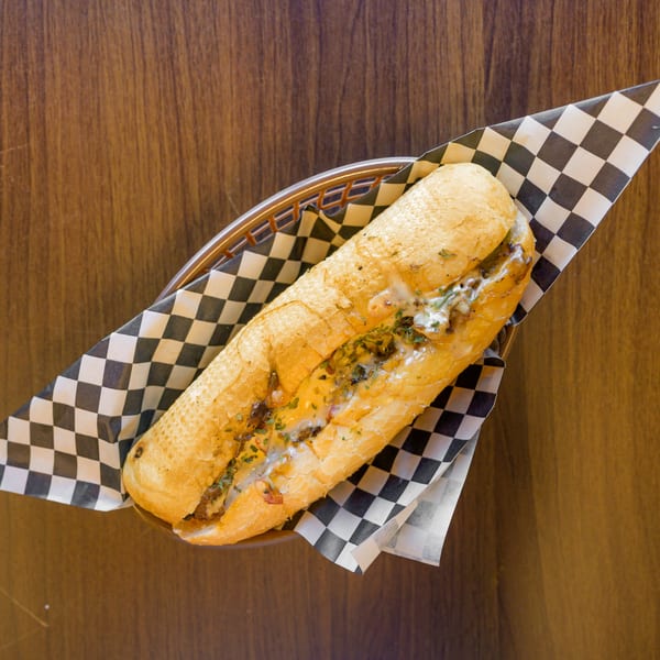 Cheesy sub sandwich with herbs in a basket lined with checkered paper on a wooden table.