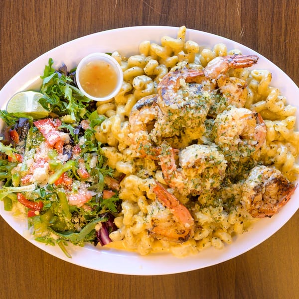 Grilled shrimp mac and cheese with a fresh green side salad and dressing on a white plate.