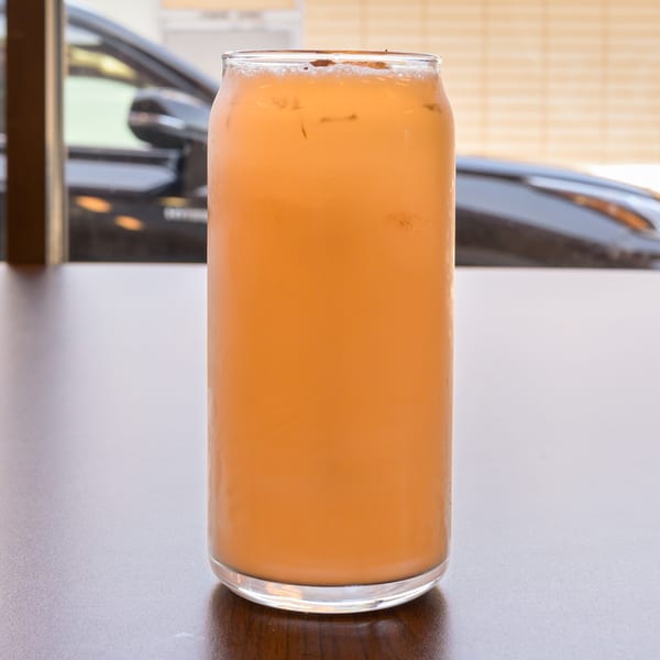 Iced peach-colored drink in a tall can-shaped glass on a table.