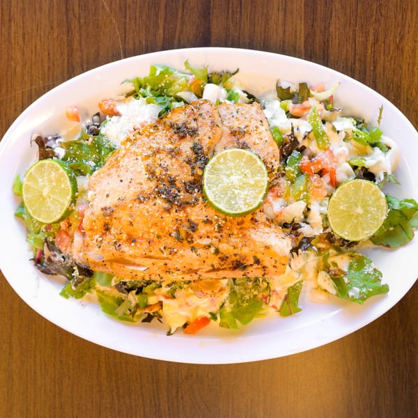 Seasoned grilled salmon with lime slices on a fresh mixed green salad with dressing.