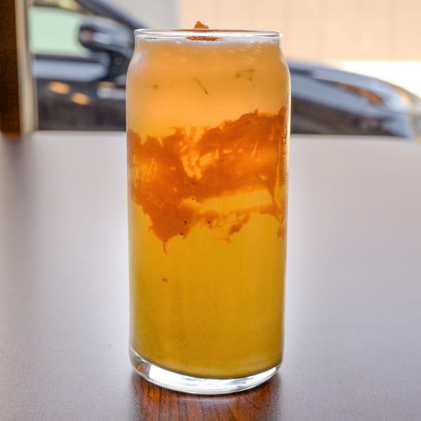 Layered yellow and orange drink in a tall glass with a topping on a table.