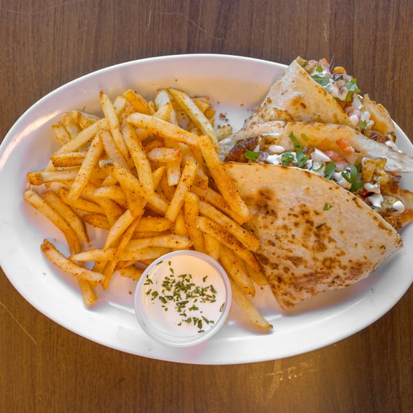 White plate with quesadilla triangles, seasoned french fries, and a cup of creamy herb dipping sauce.